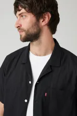 Camisa de manga corta negra con botones blancos y cuello cubano. Tiene un bolsillo en el pecho izquierdo con el logo de Levi's en rojo.