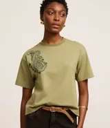 Remera boxy de algodón color verde oliva, con cuello redondo y mangas cortas. Presenta un bordado paisley en el hombro izquierdo.