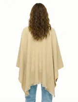 Ruana de tejido soft color beige, con cuello en V y un lazo o pasador frontal para ajustar. El ruedo tiene terminación desflecada.