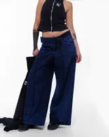 Pantalón de denim azul intenso, corte sastrero de pierna ancha, tiro alto o a la cadera (según el talle elegido), cierre frontal invisible, pretina cruzada y bordado negro del logo Temblad en la parte trasera.