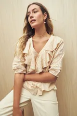 Blusa color crema con diseño calado, escote en V y volados frontales. Tiene mangas 3/4 con puños elastizados y cierre frontal con botones.