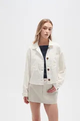 Chaqueta color blanco hueso de lino con cuello camisero, cierre frontal con botones marrones, bolsillos de parche en el pecho y corte holgado.