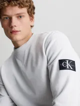Buzo gris claro de algodón con cuello redondo y ribete en V. Tiene puños y dobladillo acanalados y logo de Calvin Klein en la manga.