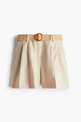 Short color beige de sarga con pinzas, tiro alto, cinturón trenzado ancho con hebilla circular, cierre con botón y corchete ocultos, bolsillos laterales discretos y bolsillos traseros insertados.