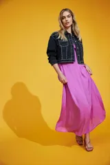 Chaqueta corta de denim negro con cuello clásico, mangas largas con puños abotonados, cierre frontal con botones y bolsillos en el pecho. Decorada con tachas plateadas.