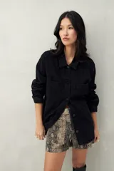 Sobrecamisa oversize de jean azul con cuello camisero, cierre frontal con botones, mangas largas y bolsillos de parche en el pecho.