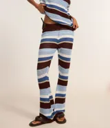 Pantalón femenino de punto con efecto crochet, de corte flare, cintura elástica y rayas horizontales en diferentes anchos y colores (azul claro, azul medio, bordó y blanco).