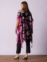 Kimono tejido con estampado floral multicolor, terminación de ruedo con borlas y mangas cortas con borde celeste.