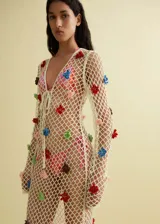 Vestido largo de tejido de punto calado color crudo, con escote en V y mangas largas. Presenta detalles de flores multicolores aplicadas.