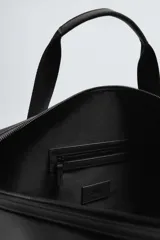 Bolso de viaje negro con acabado texturizado, compartimento principal con cierre de cremallera, bolsillo plano trasero con cierre de cremallera, banda de sujeción para equipaje y asa de hombro removible y ajustable.