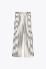 Pantalón de tiro medio con estampado de rayas verticales negras sobre fondo blanco. Tiene trabillas en la cintura, bolsillos laterales, pinzas delanteras y cierre frontal con cremallera, botón y ganchos metálicos.