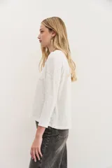 Remera blanca de algodón con calce relajado y cuello redondo. Tiene mangas largas que se ajustan hacia los puños.