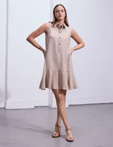 Vestido corto blanco sin mangas, con cuello camisero, abotonadura frontal parcial y ruedo con volantes.