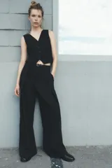 Pantalón negro de tiro medio con cinturón a tono con hebilla metálica, bolsillos delanteros y falsos bolsillos traseros.
