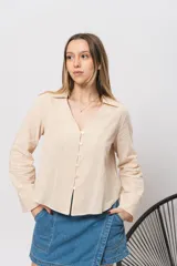 Camisa color beige de corte corto, con cuello clásico, abotonada al frente y mangas largas.