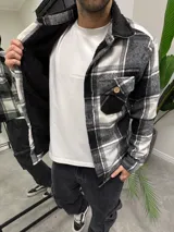 Chaqueta de paño a cuadros blancos y negros con forro interior de corderito sintético negro, cuello camisero y cierre frontal con botones de madera.