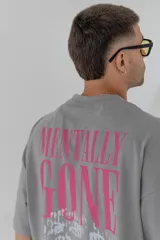 Remera gris de corte holgado con estampa en la espalda con la frase 'Mentally Gone' en rosa y un rostro abstracto en blanco.