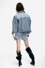Campera trucker corta de denim celeste, con cuello clásico, cierre frontal con botones metálicos, mangas largas con puños abotonados, bolsillos superiores con solapa y botón, bolsillos laterales y trabillas ajustables con botones en los laterales del bajo.