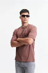 Remera marrón de manga corta con corte oversize y cuello redondo. Estampado en la espalda con diseño abstracto y texto.