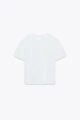 Camiseta blanca de manga corta con cuello bobo combinado a tono y acabados con fornituras a tono. Cierre en espalda con abertura y botón.