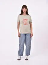 Remera blanca de algodón con cuello redondo y manga corta. Presenta un pequeño bordado en el pecho izquierdo con una figura que parece ser una persona acostada en una tabla de surf o flotador.