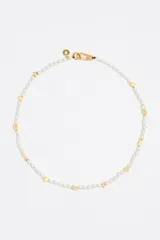 Collar corto de perlas cultivadas con dijes dorados de diferentes formas: corazón, pez, estrella, letra G y logo de la marca. Cierre de mosquetón dorado.