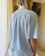 Camisa celeste de lino con mangas cortas, botones de lino y detalle drapeado en la espalda.
