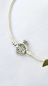Pulsera de plata con cierre de mosquetón y charm circular con logo de la marca.
