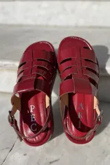 Sandalias bajas de cuero color suela, con tiras anchas entrecruzadas y hebilla lateral.