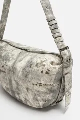 Bolso de hombro color gris con efecto desgastado, fabricado en tejido de algodón. Tiene un compartimento principal con cierre de cremallera, un bolsillo interior con cremallera y asa de hombro ajustable.