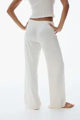 Pantalón de pijama color blanco roto, confeccionado en tejido pointelle suave. Presenta piernas levemente acampanadas, elástico revestido en la cintura con cordón fino para ajustar y ribete de volados.