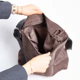 Cartera tipo bucket de cuero graneado color marrón, con correa de cuero engrasado regulable y hebilla metálica con forma de estribo. Interior 100% algodón.