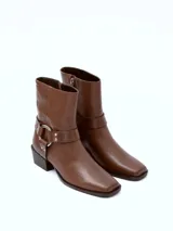 Bota de cuero negra con caña media, puntera ligeramente afilada y detalle de correa con herraje metálico circular y tachas. Taco bajo y ancho.