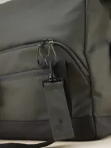 Bolso tipo duffel verde militar con base y detalles en negro. Tiene doble asa de mano y correa de hombro ajustable y extraíble. Cuenta con dos bolsillos frontales con cierre y logo de la marca en la parte inferior.