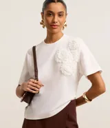 Blusa blanca de algodón con cuello redondo, mangas cortas y apliques de flores de tela en el hombro.