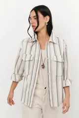 Chaqueta de algodón a rayas verticales en tonos beige y gris, con cuello camisero, cierre frontal con botones y mangas largas con puños abotonados. Tiene bolsillos delanteros con solapa y galones ondeados a tono.