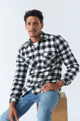 Sobrecamisa de algodón para hombre con interior de corderito, estampado a cuadros en tonos negro, blanco y azul. Tiene cierre de botones, bolsillos tipo cartera y logo en goma. El modelo usa talle M.