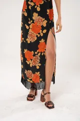 Vestido midi negro con estampado de flores naranjas y beige, espalda descubierta con tres botones en forma de flor, tajo lateral y flecos en el ruedo.