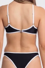 Traje de baño enterizo negro con contorno blanco, corte asimétrico y aberturas en la zona abdominal.