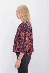 Camisa de corte amplio con estampado animal print en tonos naranja, marrón y violeta, con escote en V con lazos para atar y mangas 3/4 abullonadas.