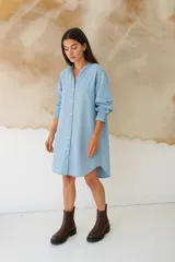 Vestido camisero corto de denim celeste, con cuello mao, mangas 3/4 con elástico en los puños y cierre frontal con botones de nácar.