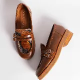 Mocasines de cuero color marrón con estampado de cocodrilo, detalle de hebilla metálica plateada y suela de goma negra. Diseño clásico con punta redonda y calce cómodo.