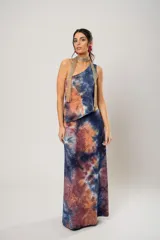 Conjunto de falda larga y top asimétrico con estampado tie-dye en tonos azul, naranja y marrón. El top es de un solo hombro y tiene un collarín con flecos dorados.