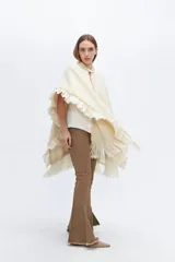 Ruana tejida en lana merino con detalles de lino, con flecos delicados y paleta de colores neutros.