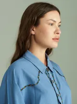 Camisa celeste de algodón con corte clásico y caída suelta. Presenta vivos en cuadrillé trazados en puños, canesú de la espalda y al pie del cuello.