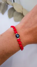 Pulsera elástica con cuentas rojas en forma de corazón, separadores plateados y un dije central de ojo turco.