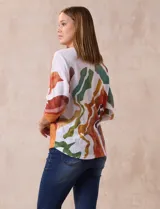 Buzo blanco con estampado abstracto en tonos naranja, verde, marrón y rojo. Tiene cuello redondo y mangas 3/4.