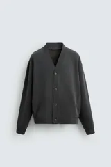 Cárdigan gris oscuro de corte holgado confeccionado en tejido de mezcla de algodón con interior perchado. Presenta cuello en V, manga larga, bolsillos de vivo en la cadera, acabados en rib y cierre frontal con botones.