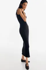 Vestido maxi negro sin mangas, de corte ajustado, con escote redondo y detalle de frunces drapeados en el lateral. El tejido presenta una textura sutilmente arrugada o gofrada.