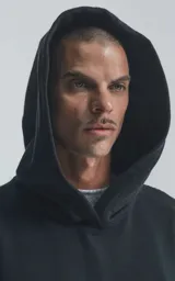 Hoodie negro de corte oversize con capucha, bolsillo tipo canguro y detalle de bolsillo con cierre en la manga izquierda.